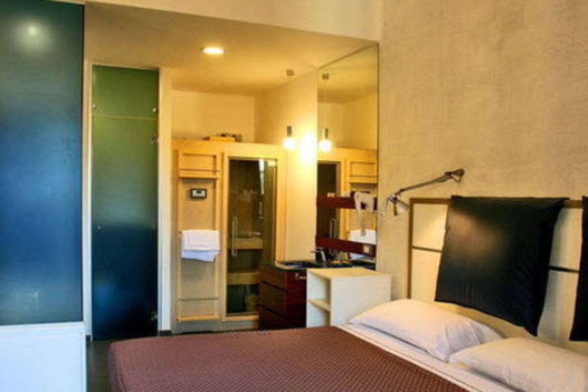 A hotel room with a bed, a desk, a mirror, and a bathroom visible through an open door.