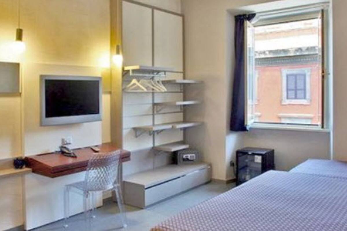 A hotel room with a bed, a desk, a chair, a TV, and a window with a view of a building.