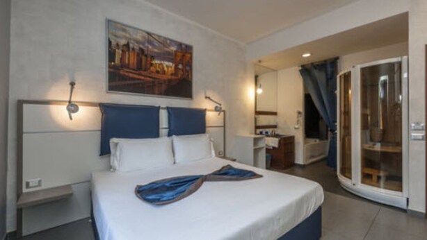 Ein modernes Hotelzimmer mit einem großen Bett, einem Schreibtisch, einem Badezimmer und einer Glastür zum Balkon.