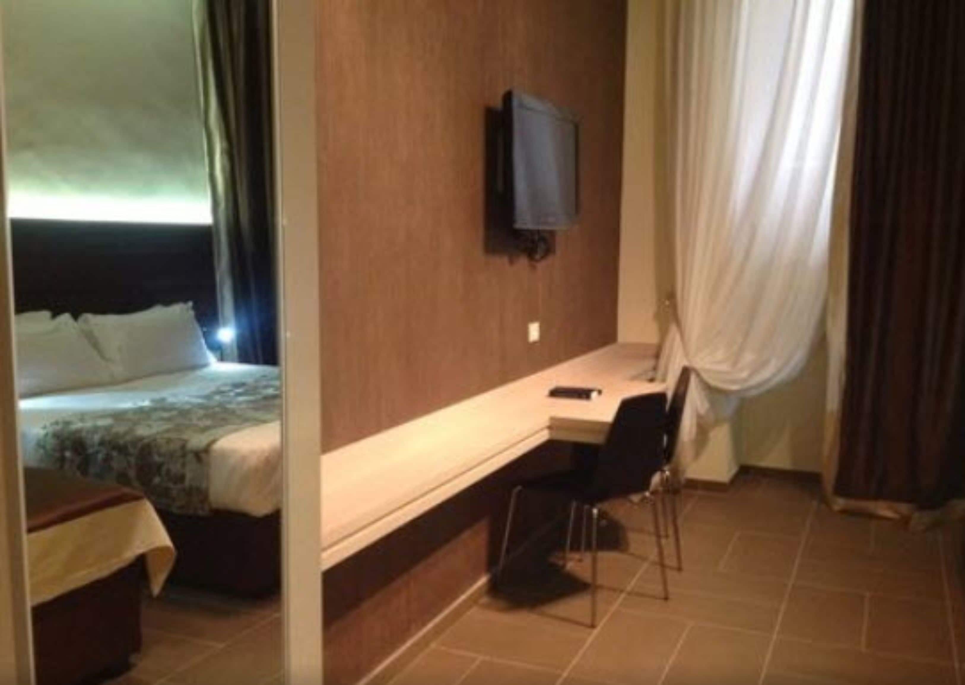 A hotel room with a bed, a desk, a chair, a television, and curtains.