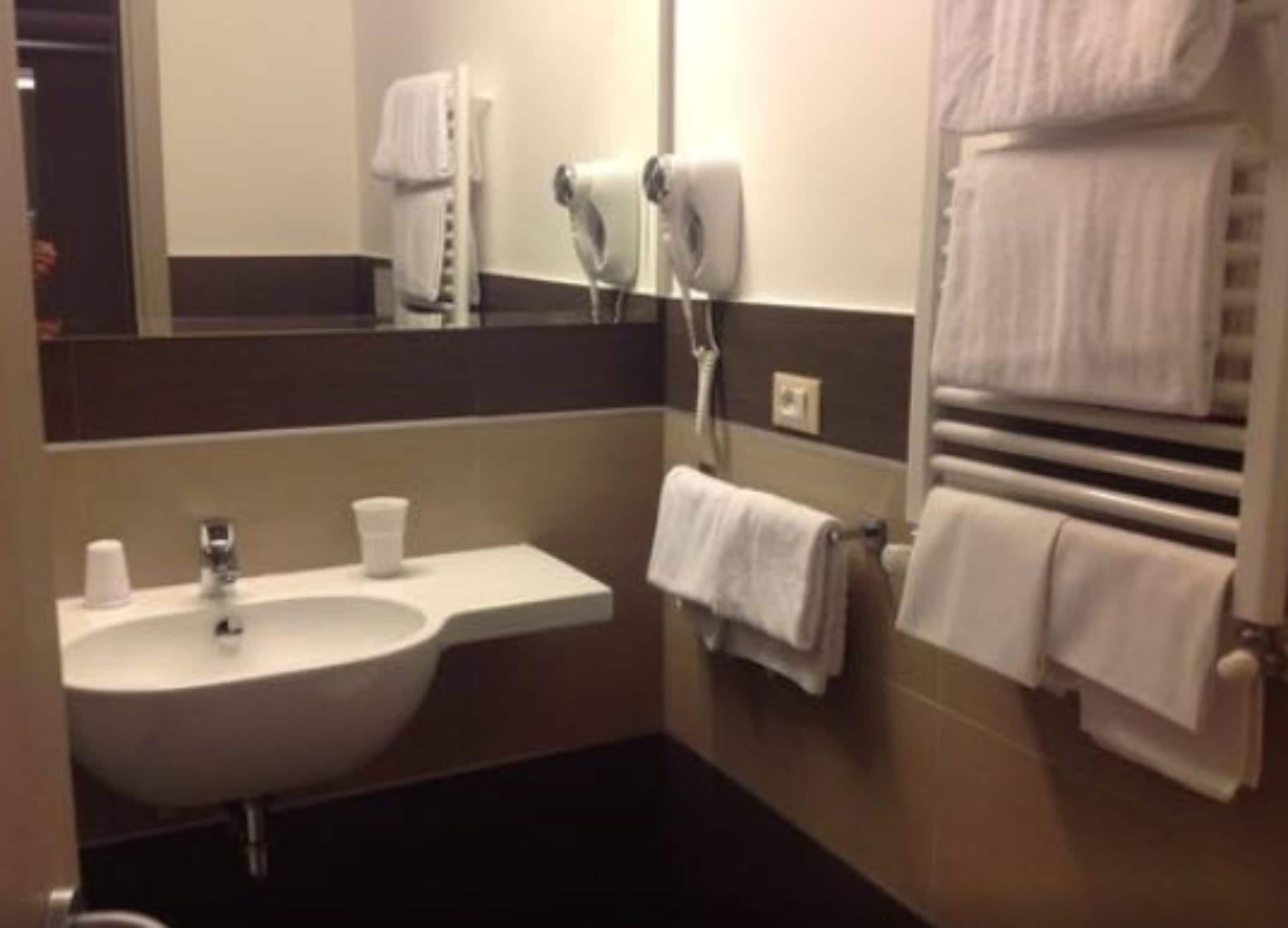 A bathroom with a sink, hand dryer, and stacked towels.