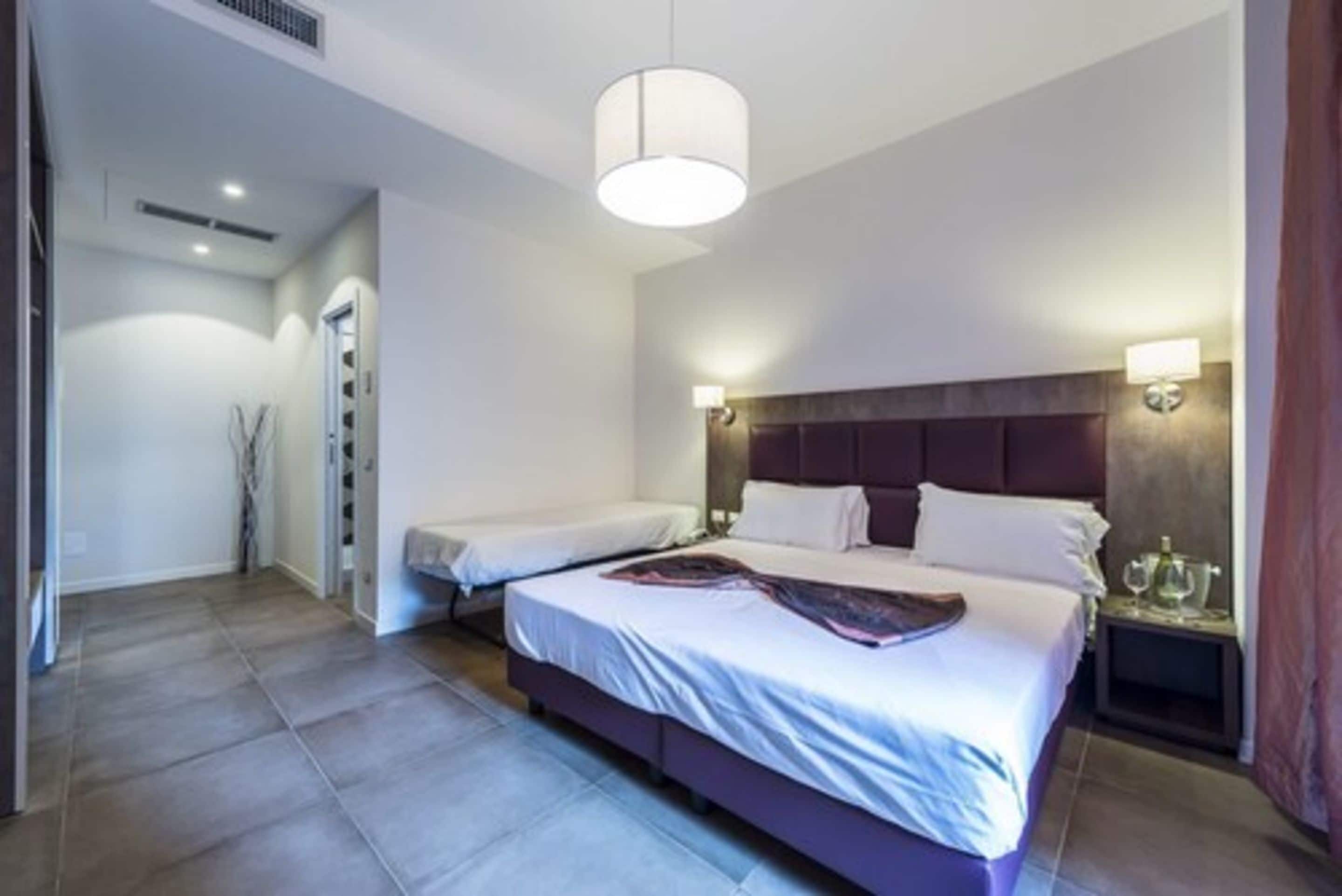 A modern hotel room with a large bed, bedside tables, a headboard with integrated lighting, and a visible closet.
