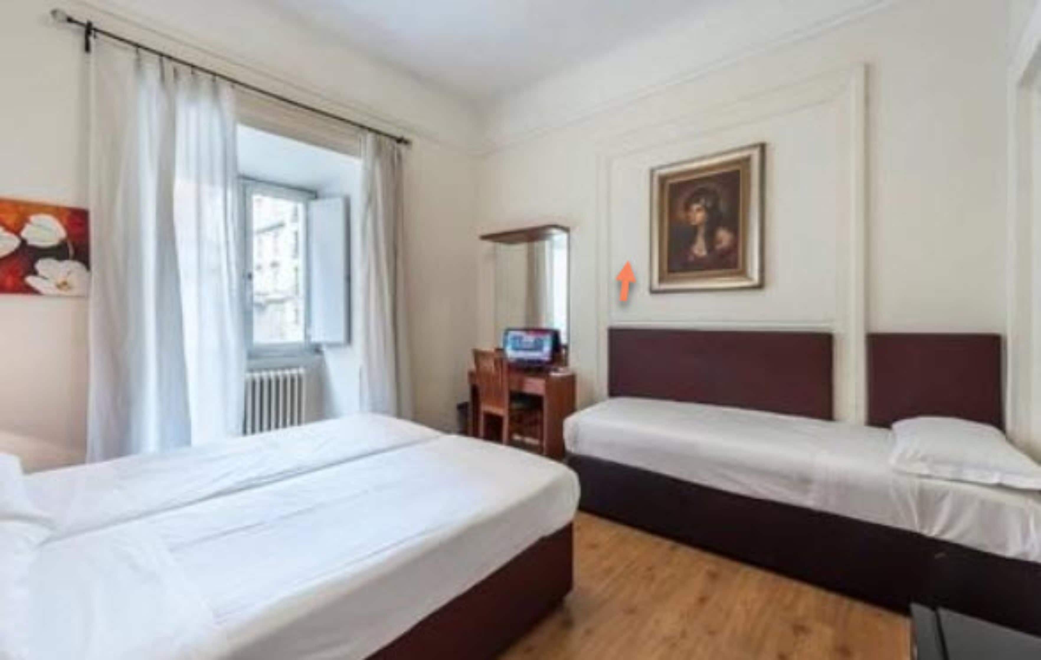 A hotel room with two beds, a desk with a computer, a window with curtains, and a painting on the wall.