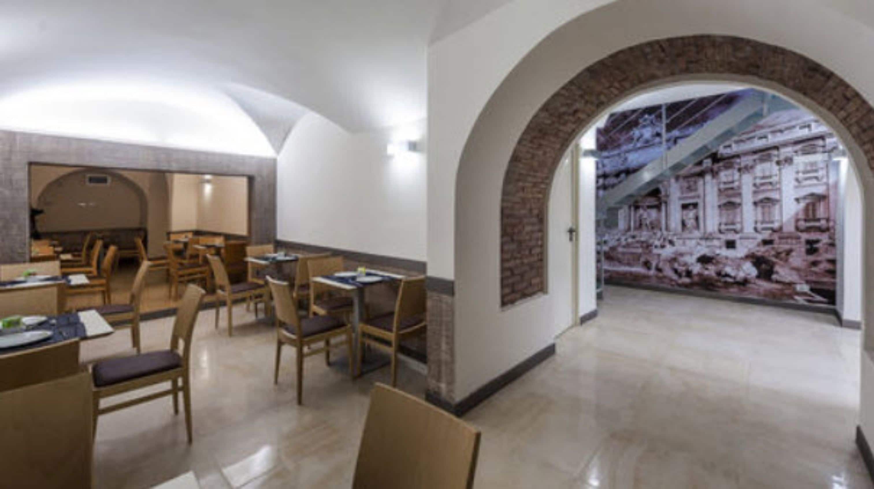A spacious dining area with wooden tables and chairs, a large mural on the wall, and a stone archway leading to another room.