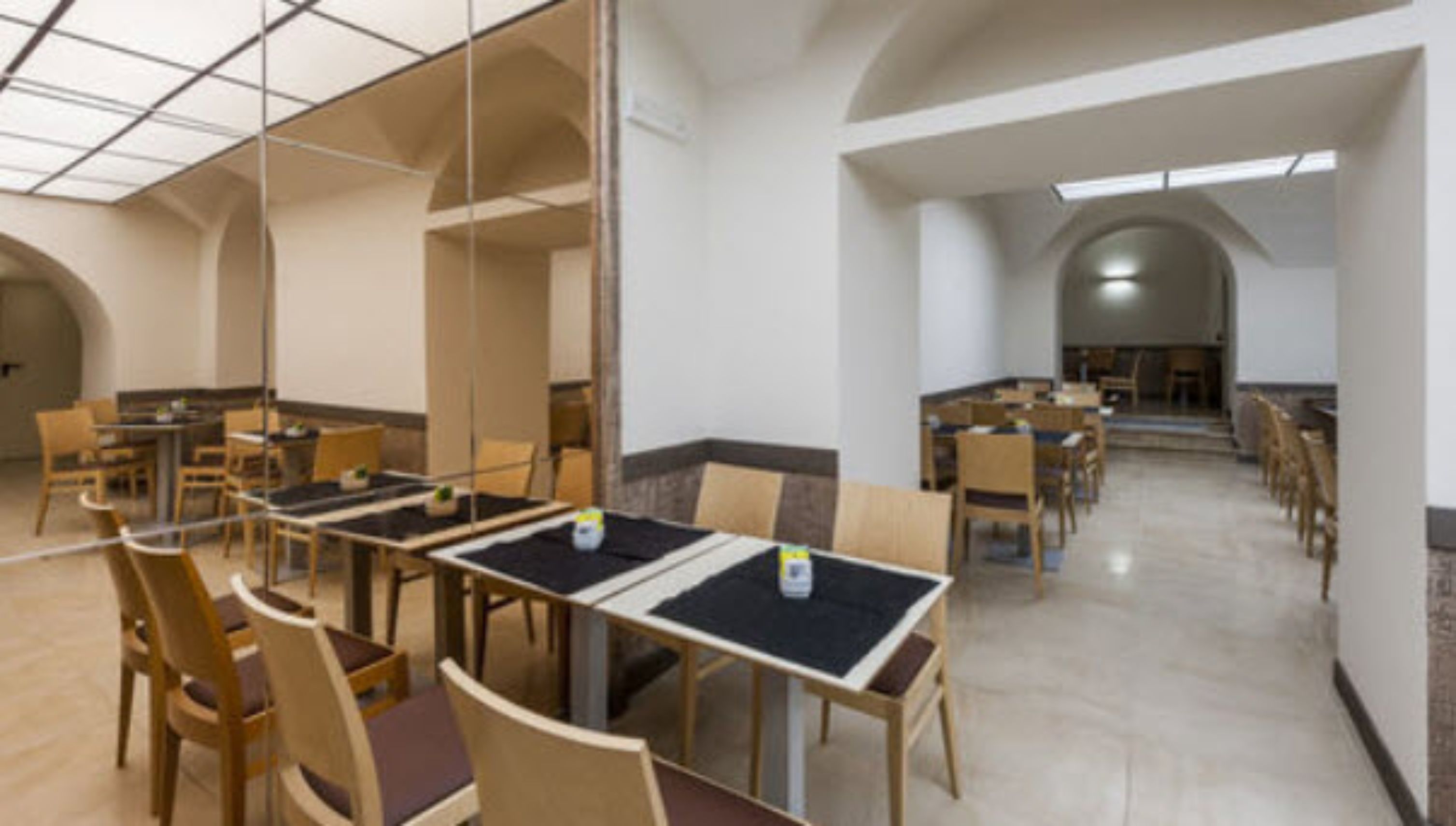 A dining area with tables and chairs, high ceilings, and arched doorways.