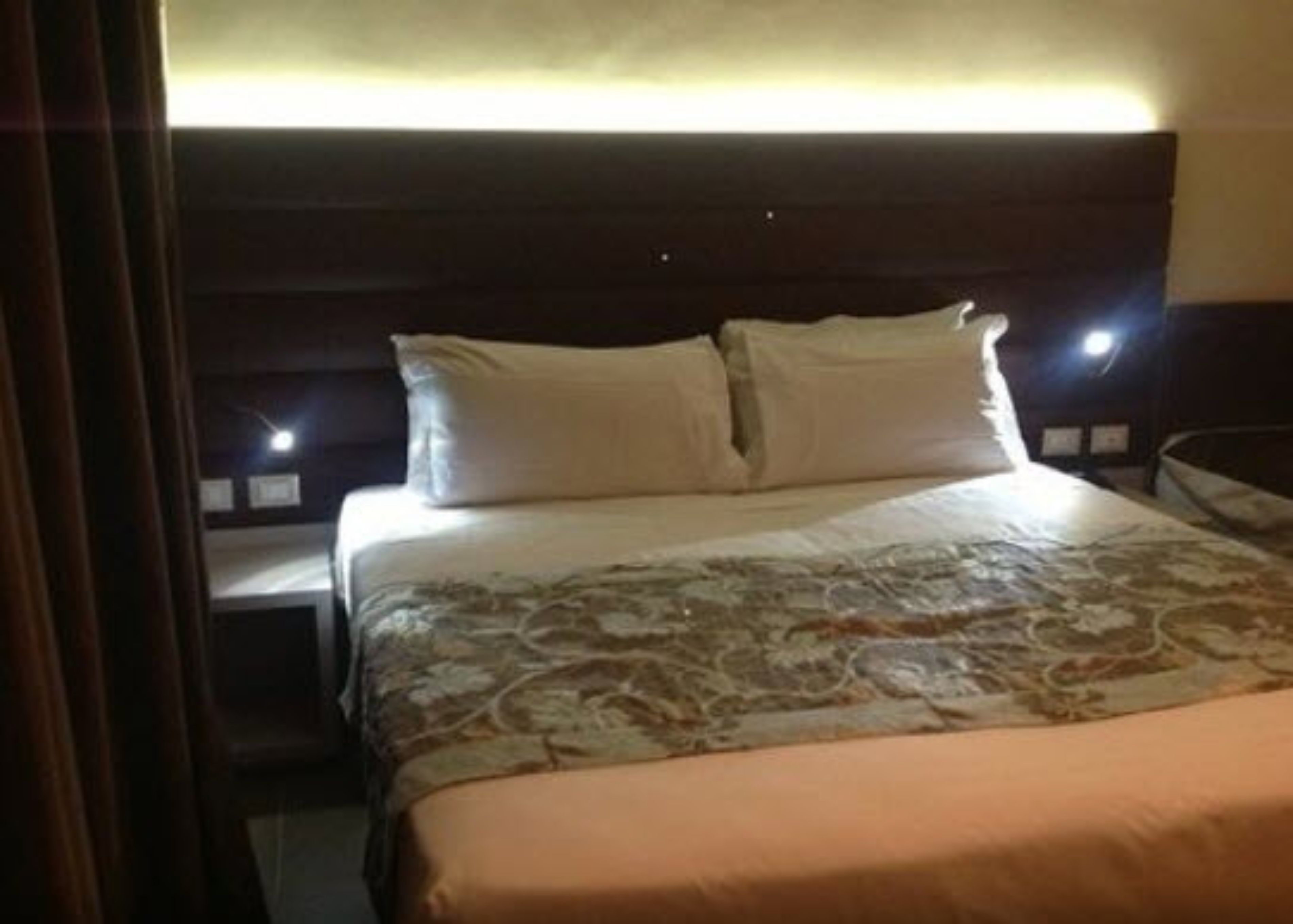 A hotel room with a large bed, a headboard, and two bedside lamps.