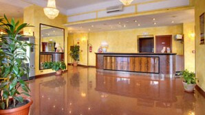 Eine Hotelhalle mit glänzendem Boden, einer Rezeption und mehreren Blumentöpfen.