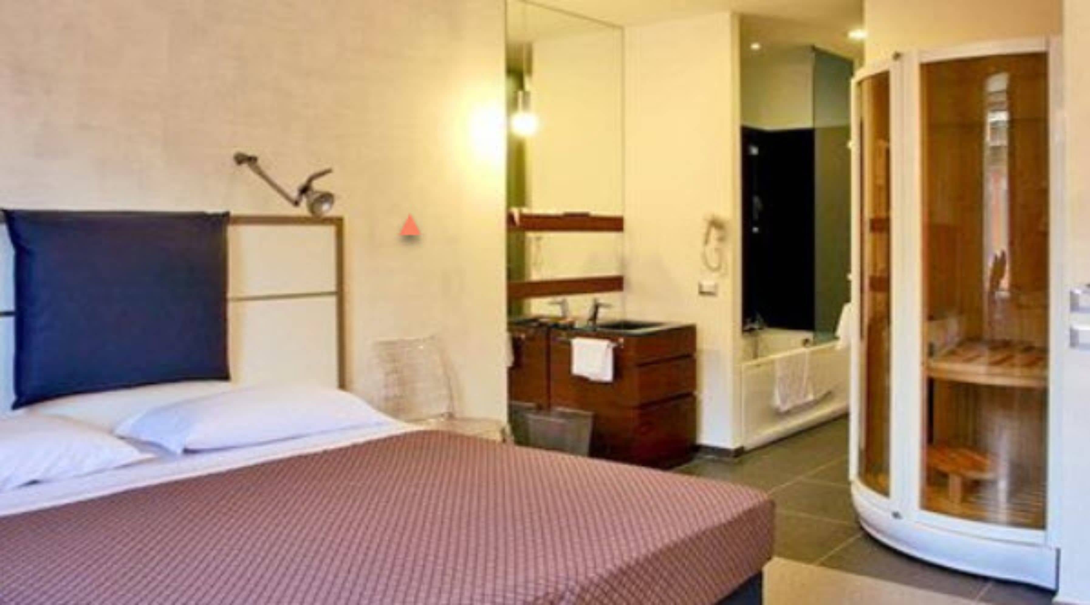 Ein Hotelzimmer mit Bett, Schminktisch, Spiegel und einem durchgegangenen Tür einsehbaren Badezimmer.