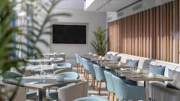 Un restaurante moderno con una barra larga, sillas azules y una planta grande en maceta.