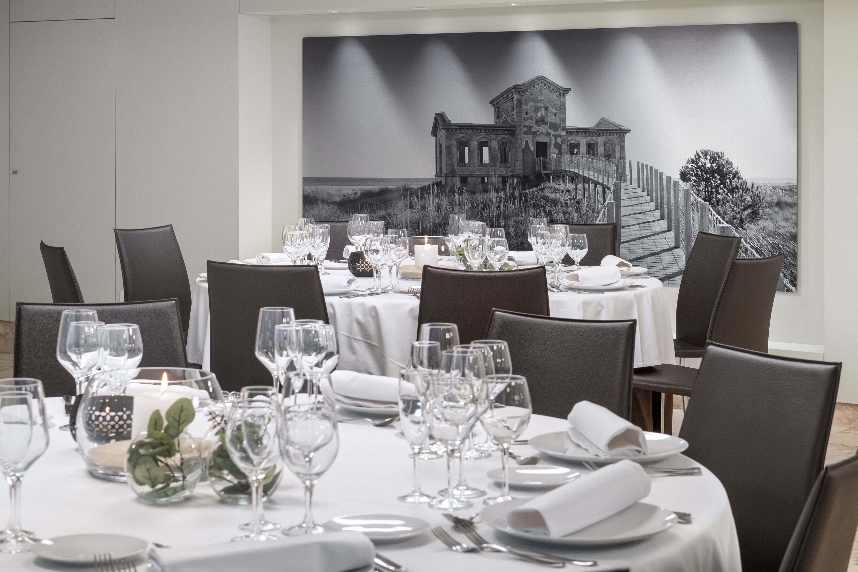 A dining area with round tables set for a meal, each with white tablecloths, clear glassware, and neatly folded napkins.
