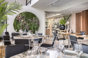Un espace repas moderne avec des tables rondes, des chaises noires et un grand mur végétal.