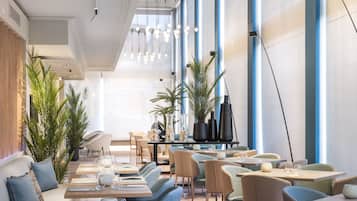 Interior moderno de restaurante con techos altos, iluminación colgante y diversas opciones de asientos, incluyendo mesas y sillas.