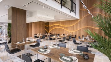 Un comedor moderno con varias mesas y sillas, que presenta una pared de acento de madera y un techo de cristal.