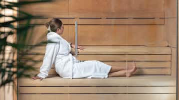 Eine Person in einem weißen Bademantel sitzt auf Holzstufen in einer Wellness-Umgebung.