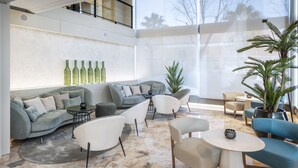Un área de estar moderna con un sofá curvo, sillones blancos, suelo de mármol y un ventanal con vistas a árboles.