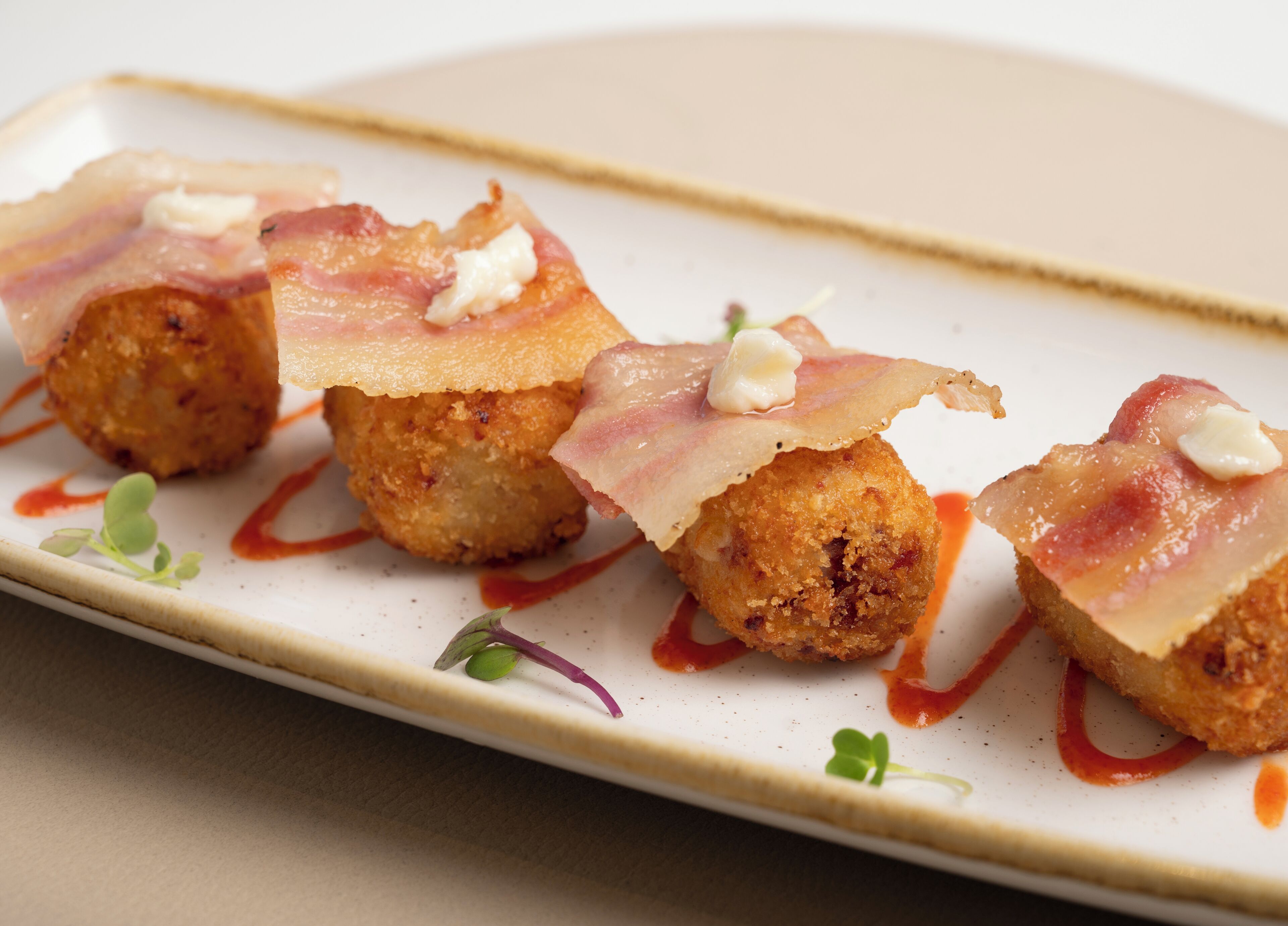 A plate of food with crispy balls topped with bacon and a drizzle of sauce.