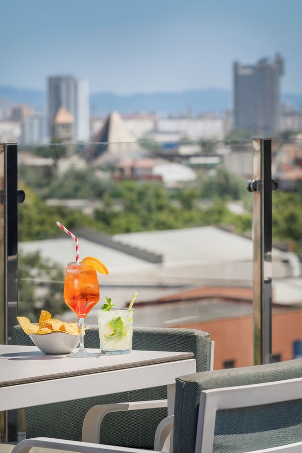 Une table avec deux boissons, un bol de chips et, en arrière-plan, une vue sur la ville.