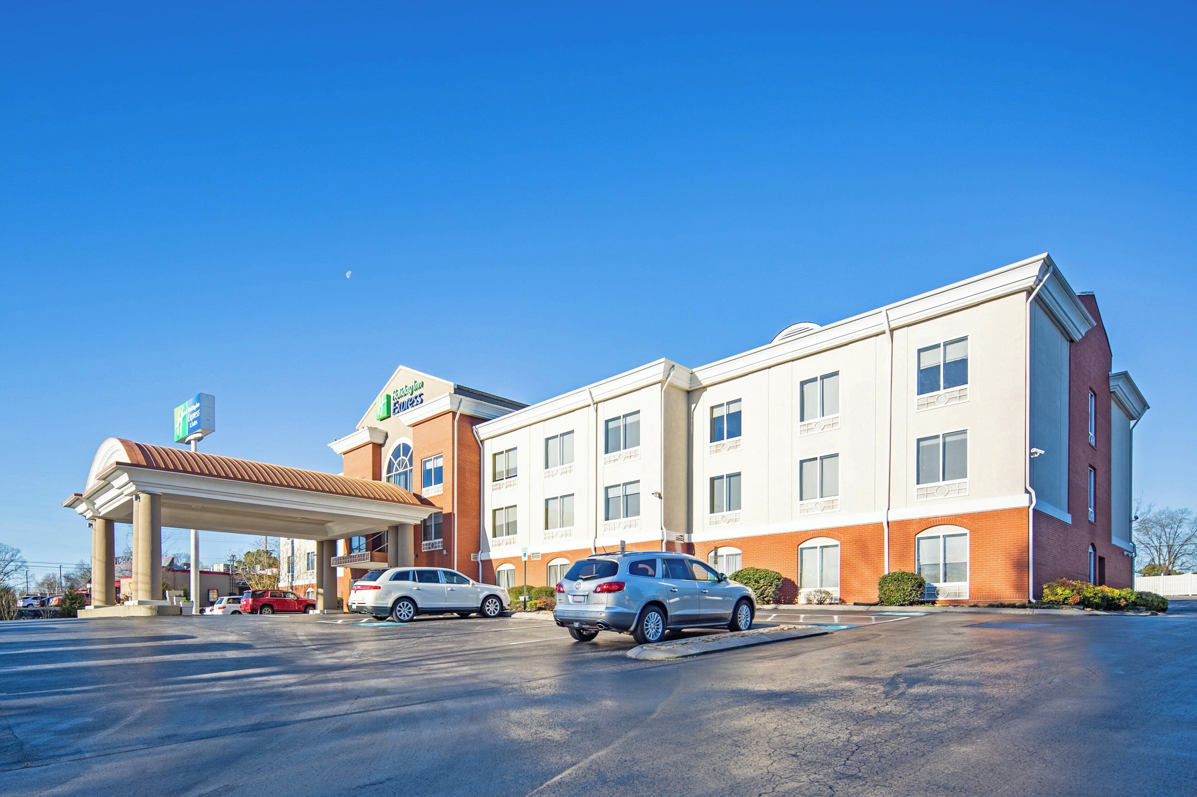 A hotel with a covered parking area, multiple cars parked, and a clear blue sky.