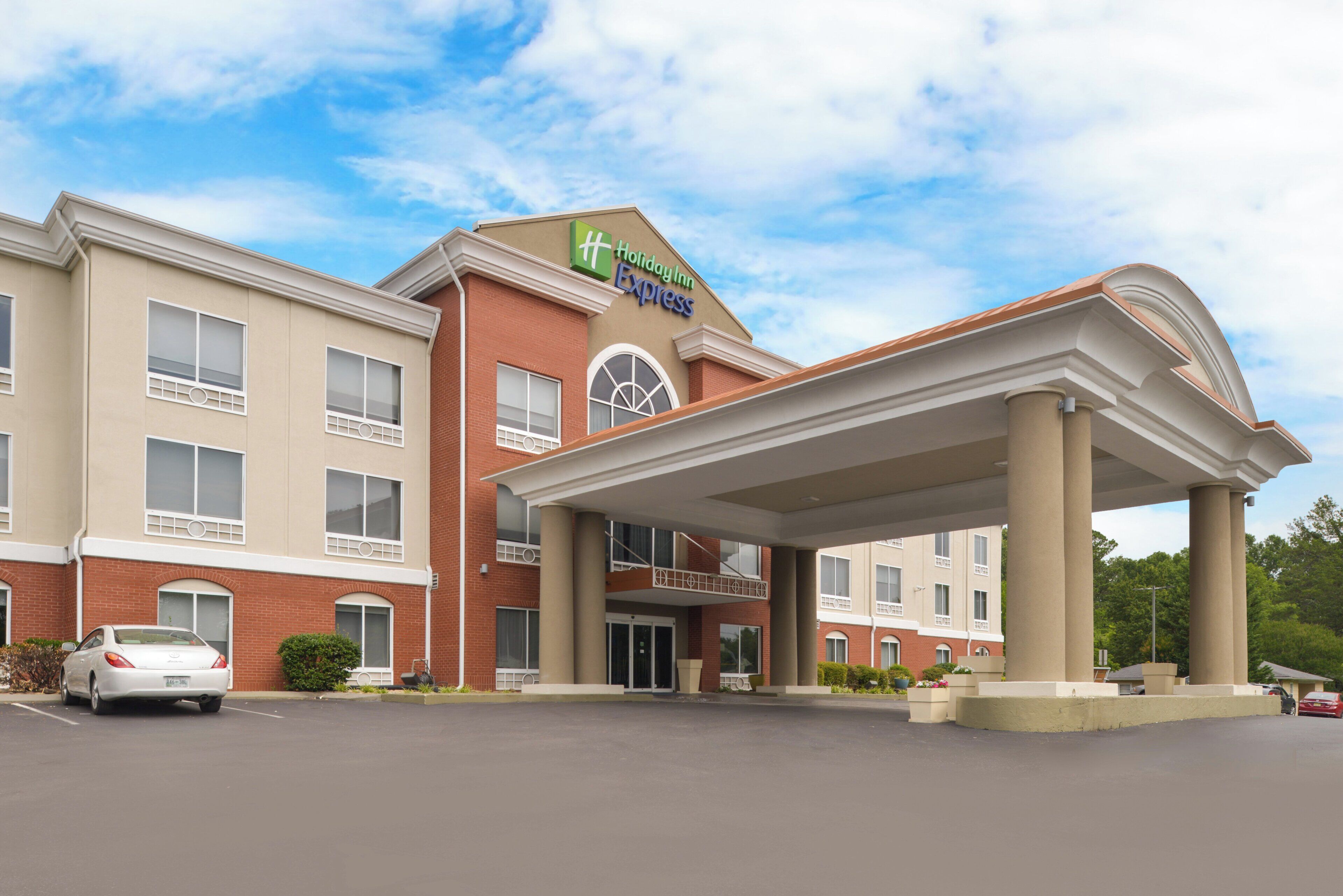 Un hotel Holiday Inn Express con entrada techada, fachada de ladrillo y estacionamiento.