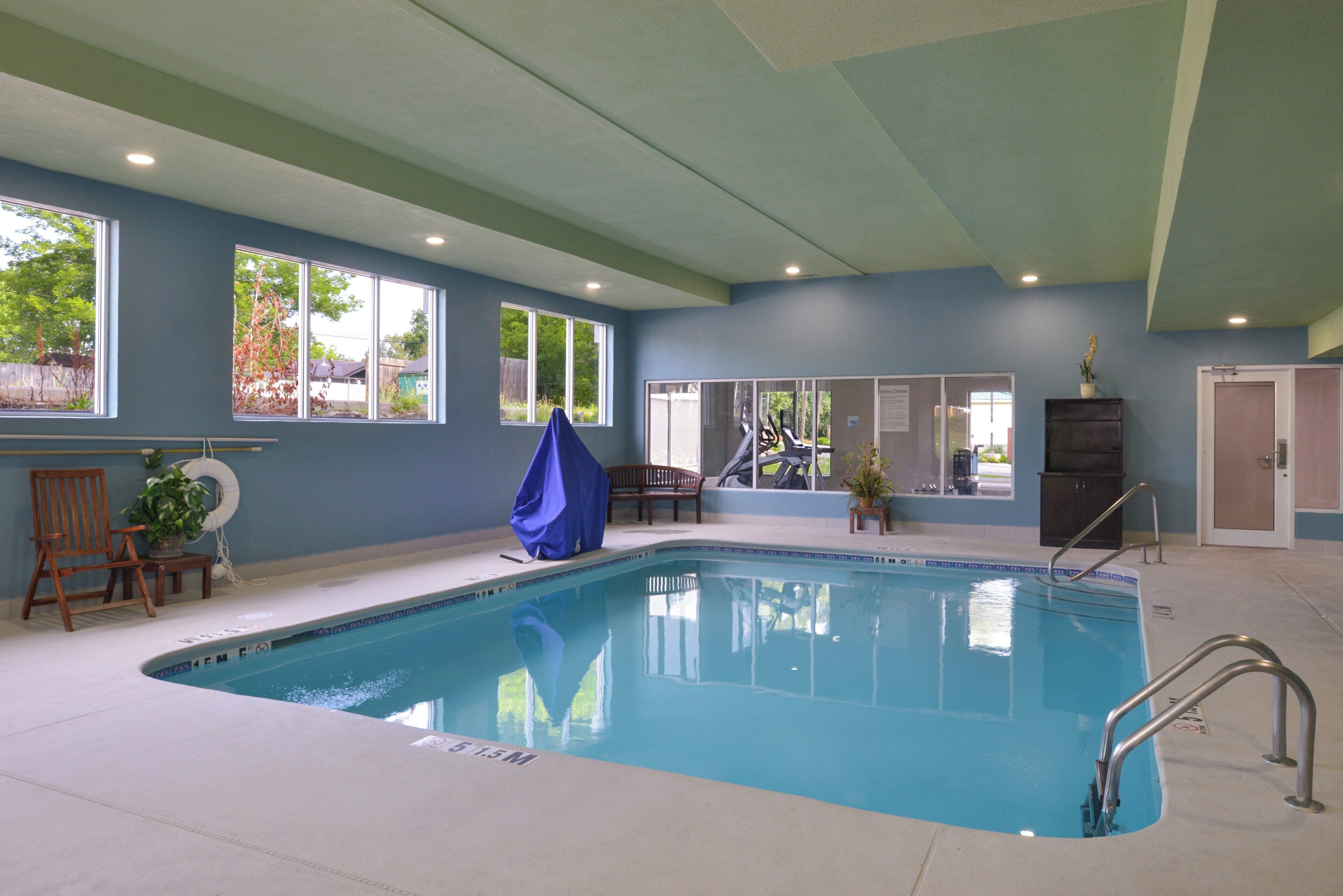 Una piscina interior con agua cristalina, rodeada de ventanas, una silla de madera y un banco.