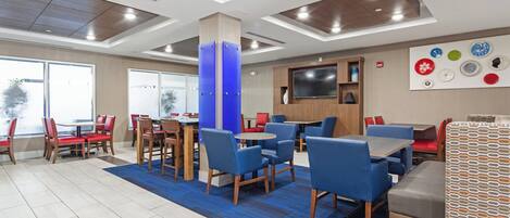 A modern dining area with multiple tables and chairs, a flat-screen TV mounted on the wall, and a blue carpet.