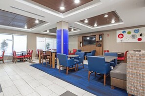 A modern dining area with multiple tables and chairs, a flat-screen TV mounted on the wall, and a blue carpet. - Holiday Inn Express & Suites Chattanooga (East Ridge) by IHG (Chattanooga)