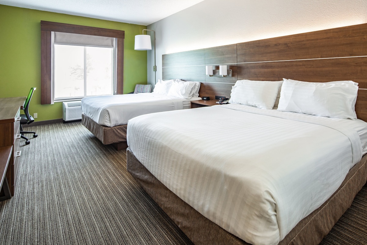 Une chambre d’hôtel avec deux lits, un bureau, une lampe et une fenêtre.
