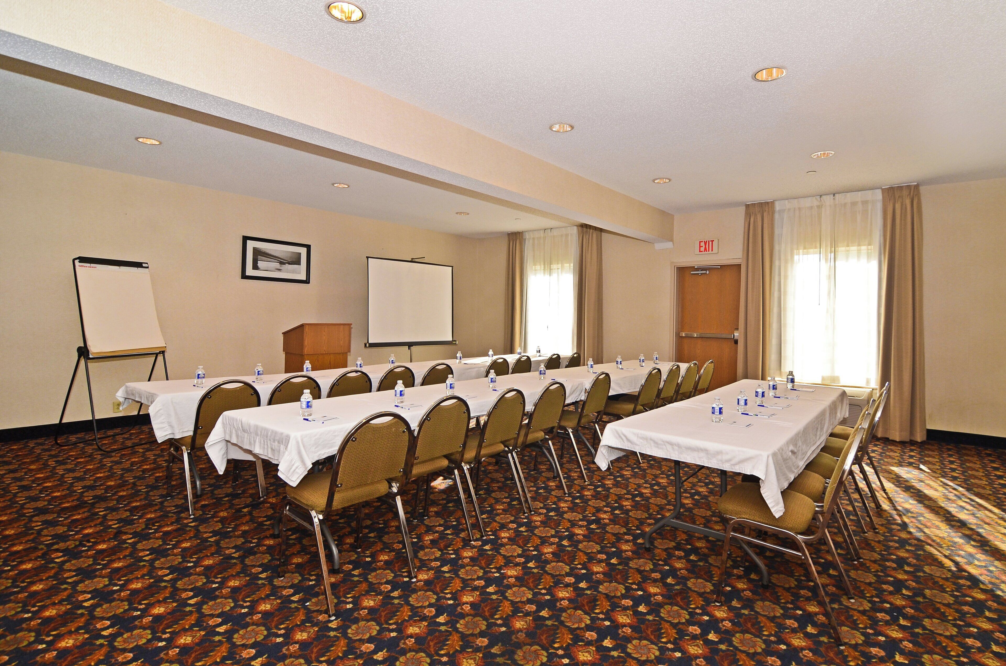 A conference room with multiple tables, chairs, a whiteboard, and an exit sign.