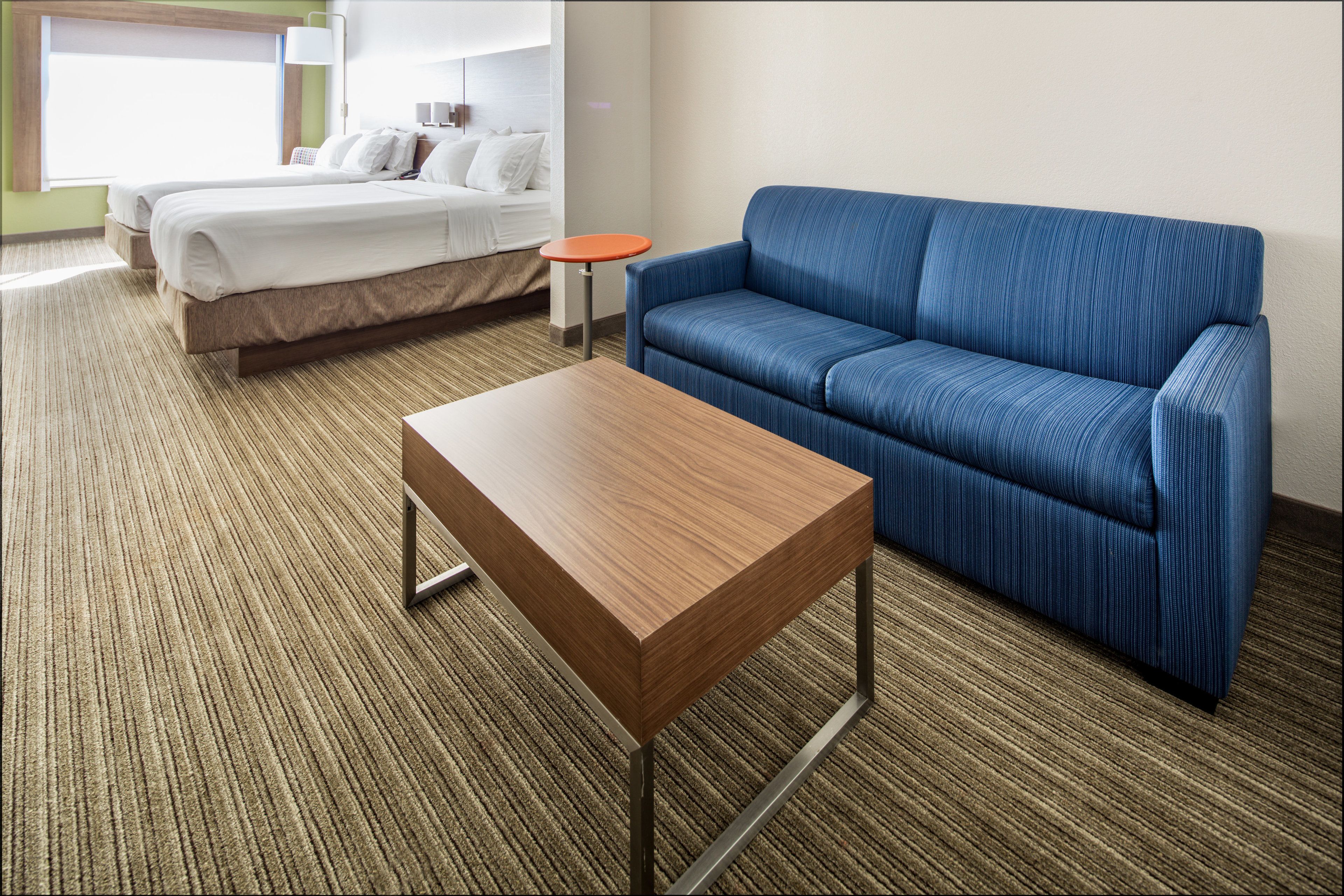 A hotel room with a bed, a blue sofa, and a wooden table.