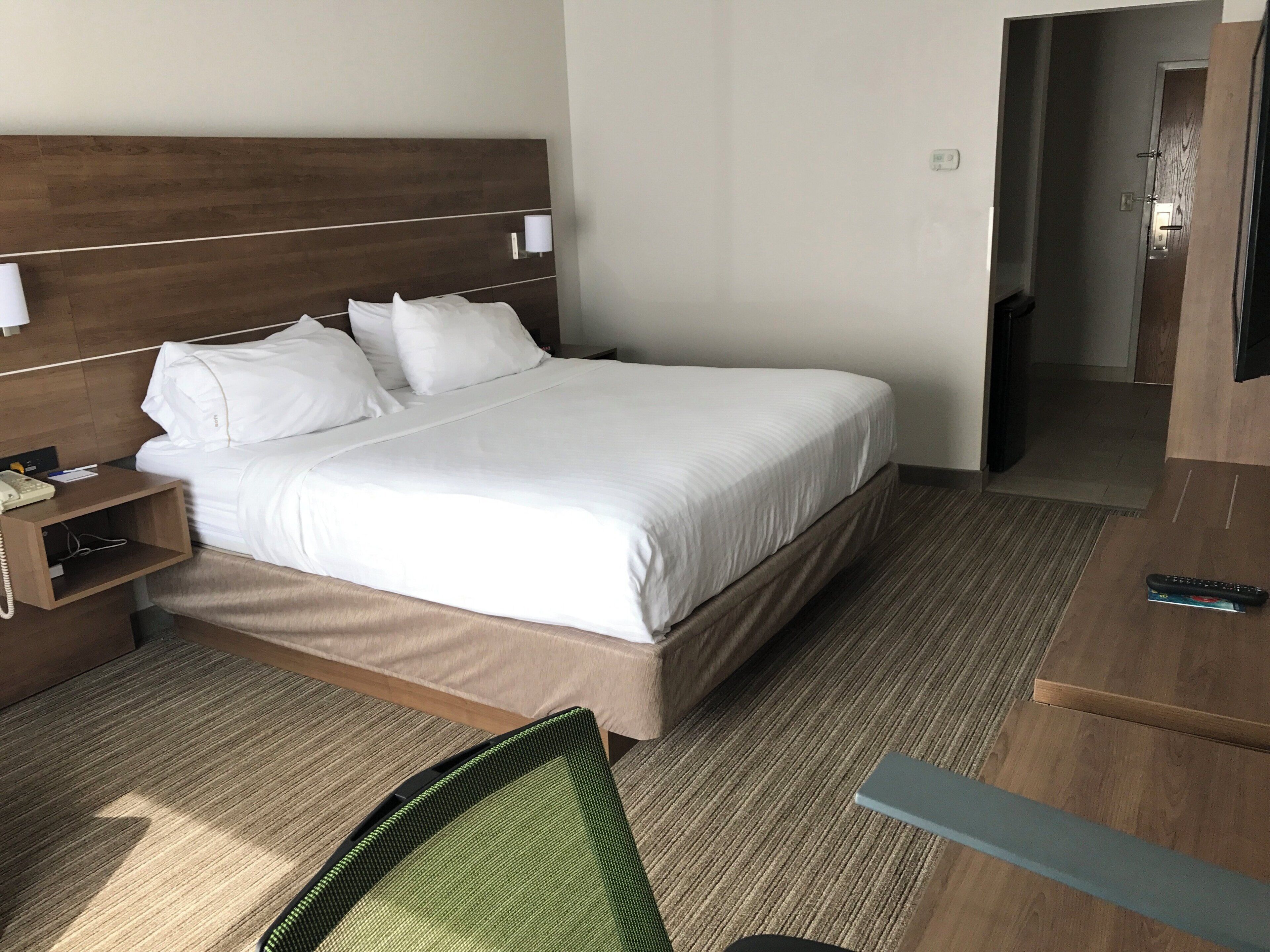 A hotel room with a bed, bedside table, lamp, and a television.