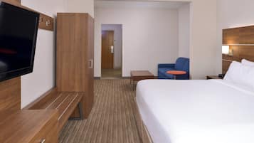 Habitación de hotel con cama, televisión, zona de estar con una silla y una mesita, y un armario de madera.