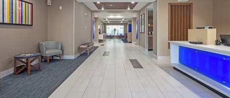 A hotel lobby with a reception desk, seating area, and a corridor leading to other rooms.