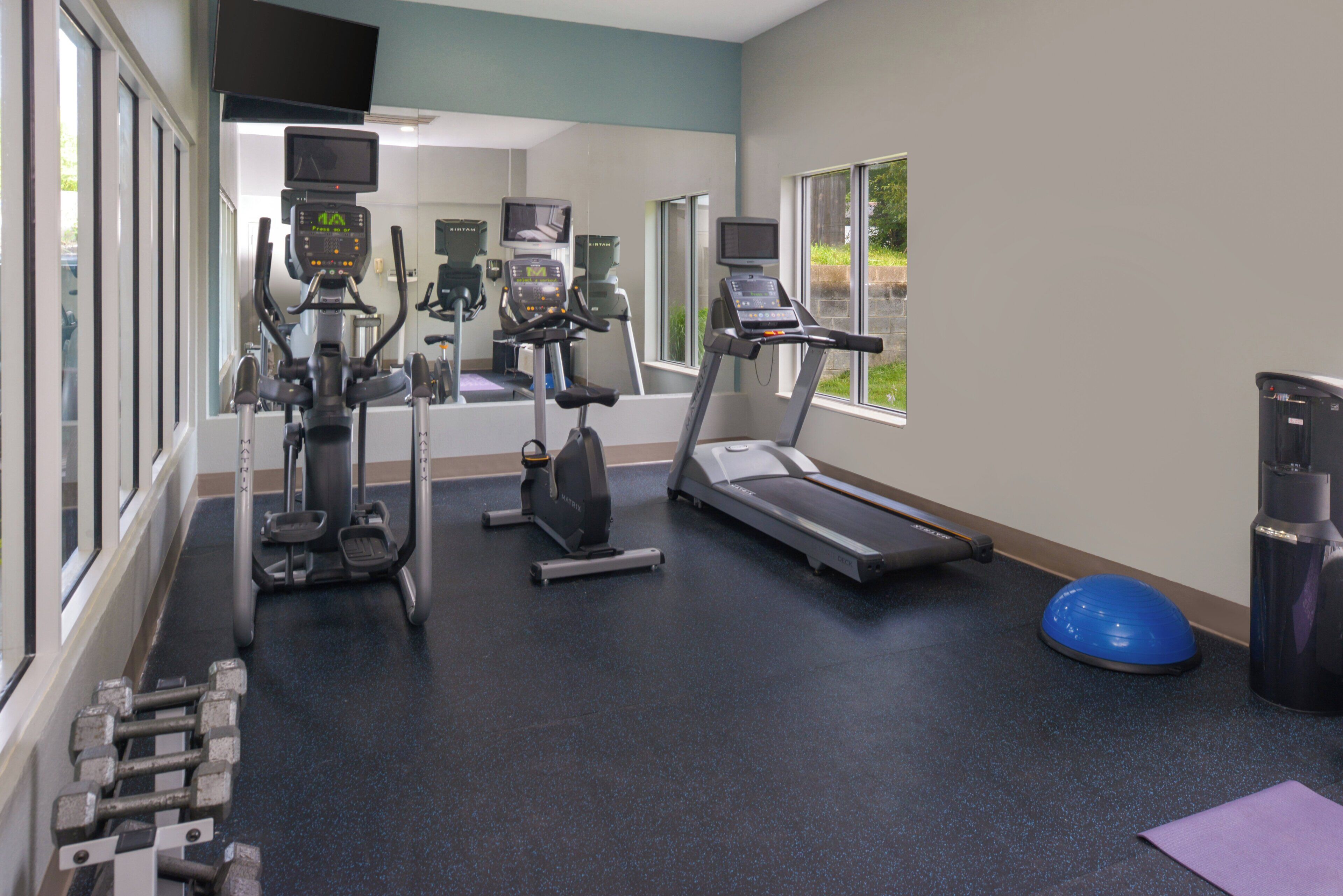 A gym with cardio machines, dumbbells, and a blue exercise ball.