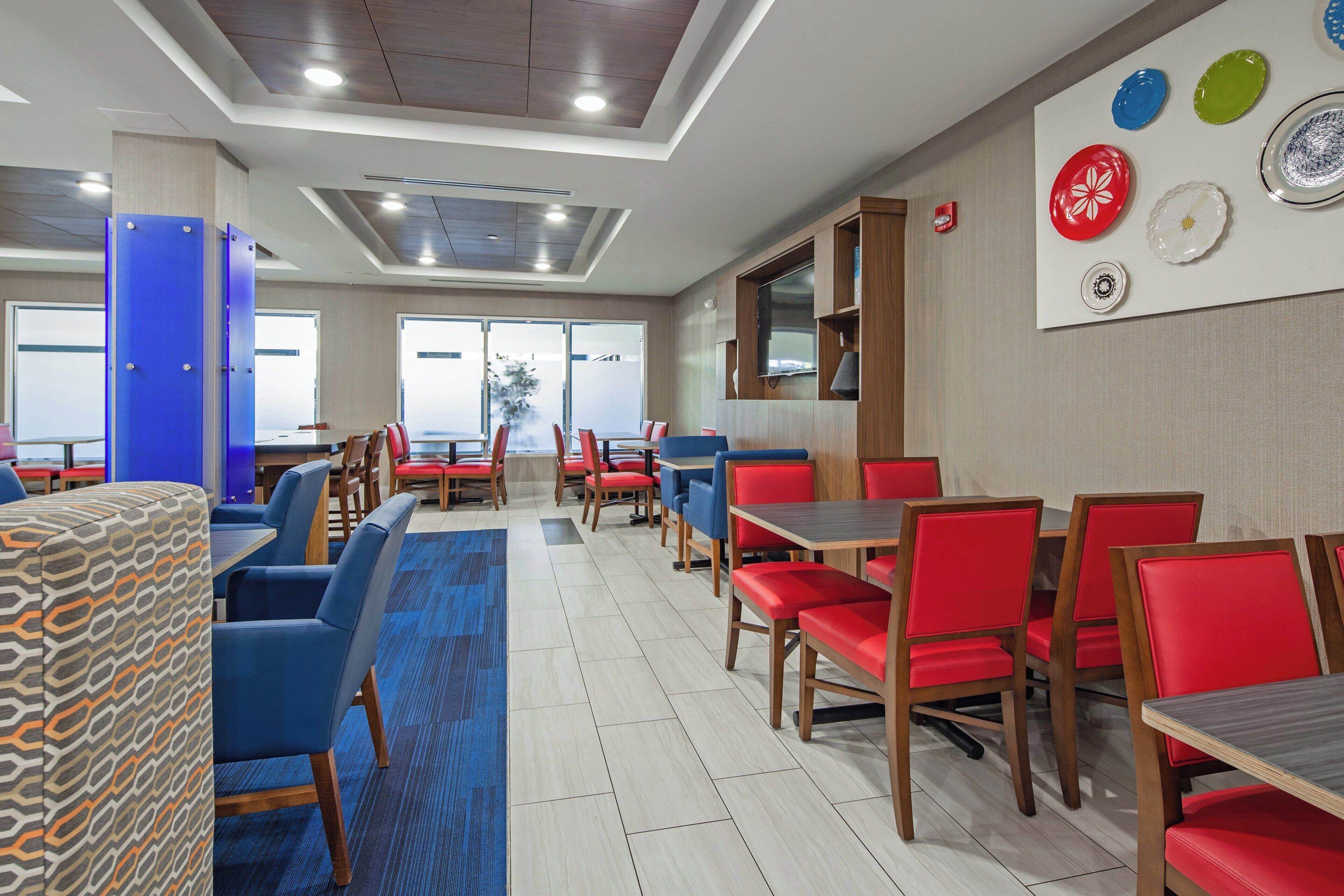 A modern dining area with multiple tables and chairs, a flat-screen TV mounted on the wall, and a patterned carpet.