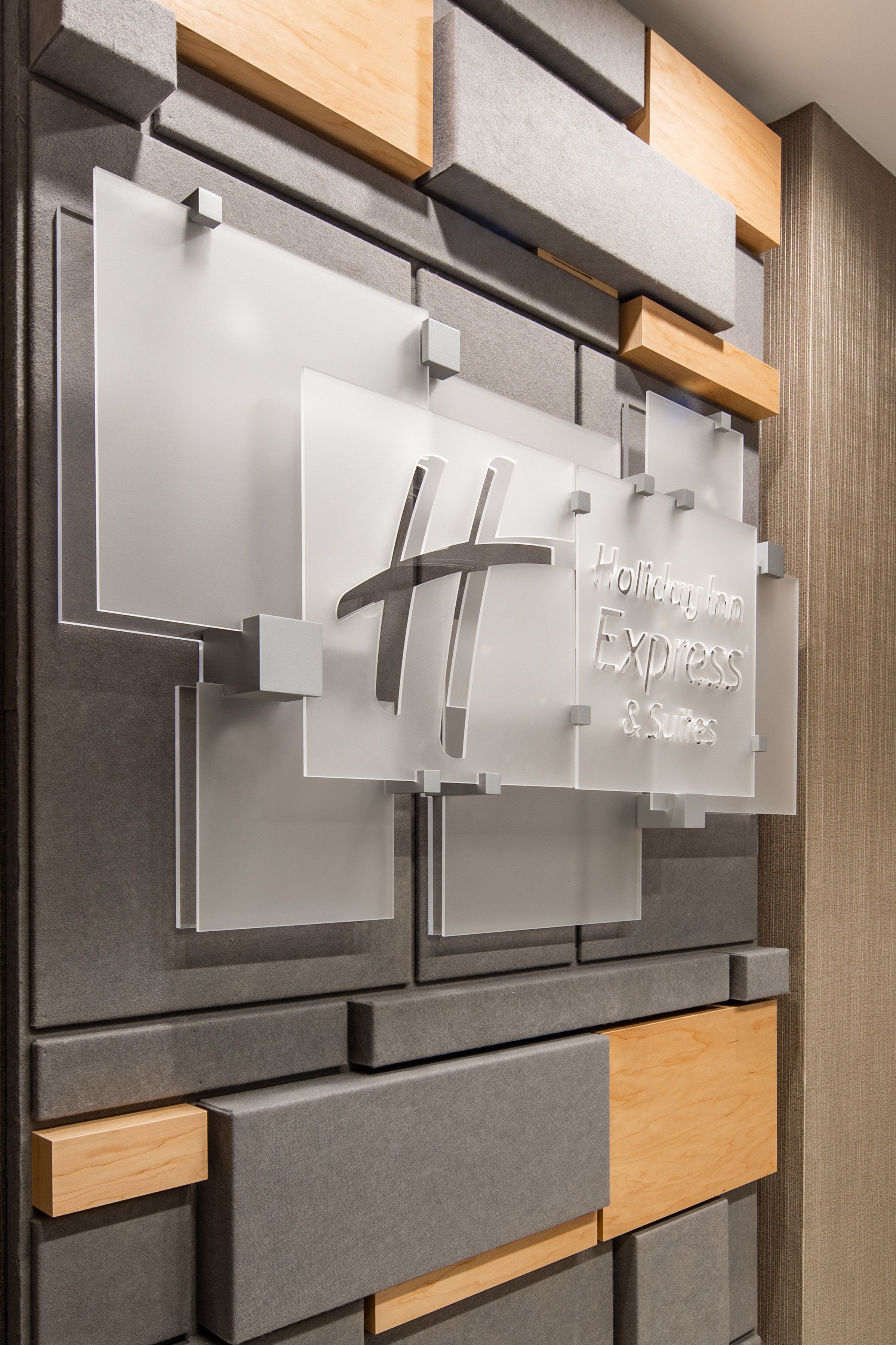 A wall with a sign for Holiday Inn Express & Suites, featuring a modern design with grey and wooden elements.