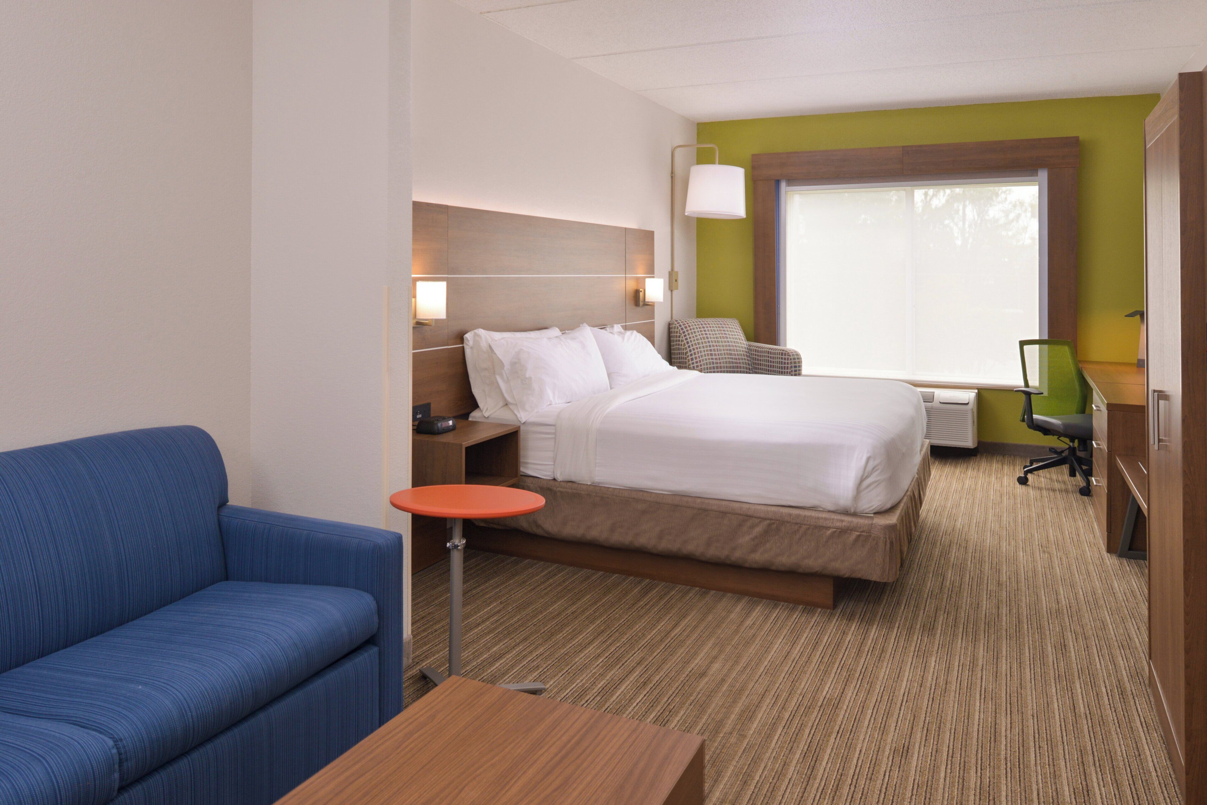 Une chambre d’hôtel avec un lit, un canapé bleu, une petite table, un bureau et une fenêtre.