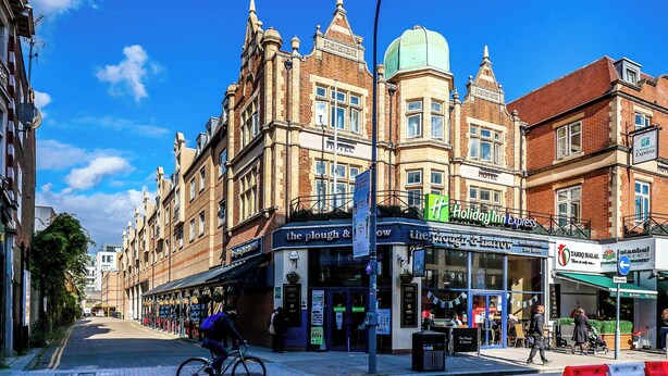 A street view with a building featuring a Holiday Inn Express sign, a restaurant named 'The Plough & Harrow,' and a TARIQ HALAL restaurant.