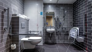 Moderni kylpyhuone, jossa on harmaat laatat, wc-istuin, pesuallas ja suihku.