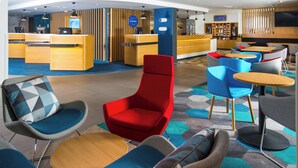 A modern hotel lobby with a reception desk, seating area, and a television screen.