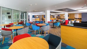 A modern hotel lobby with multiple seating areas, a reception desk, and a bar.