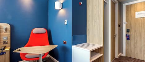 Una habitación de hotel con una pared azul, una silla roja, un escritorio de madera y un armario de madera.