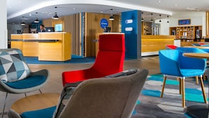 A modern hotel lobby with a reception desk, seating area, and a coffee bar.