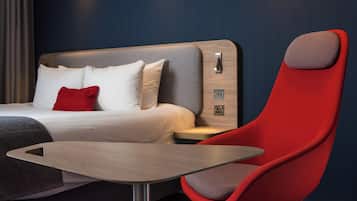 Une chambre d’hôtel moderne avec un lit, une table de chevet et un fauteuil rouge.