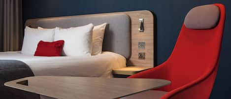 A modern hotel room with a bed, bedside table, and a red chair.