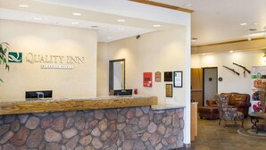 A hotel reception area with a stone counter, a reception desk, a mirror, framed awards, and a seating area with chairs and a table.