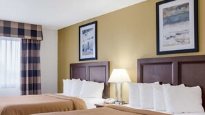 A hotel room with two beds, a lamp, and two framed pictures on the wall.