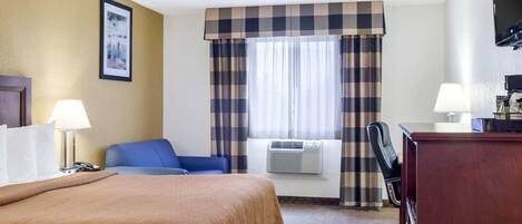Une chambre d’hôtel équipée d’un lit, d’un bureau, d’une chaise, d’une lampe, d’un climatiseur et d’une fenêtre avec des rideaux.