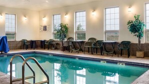 An indoor swimming pool with multiple chairs and tables, surrounded by windows and wall-mounted lights.
