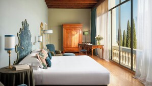 A bedroom with a large bed, a wooden cabinet, a desk with a chair, and a view of trees through a window.