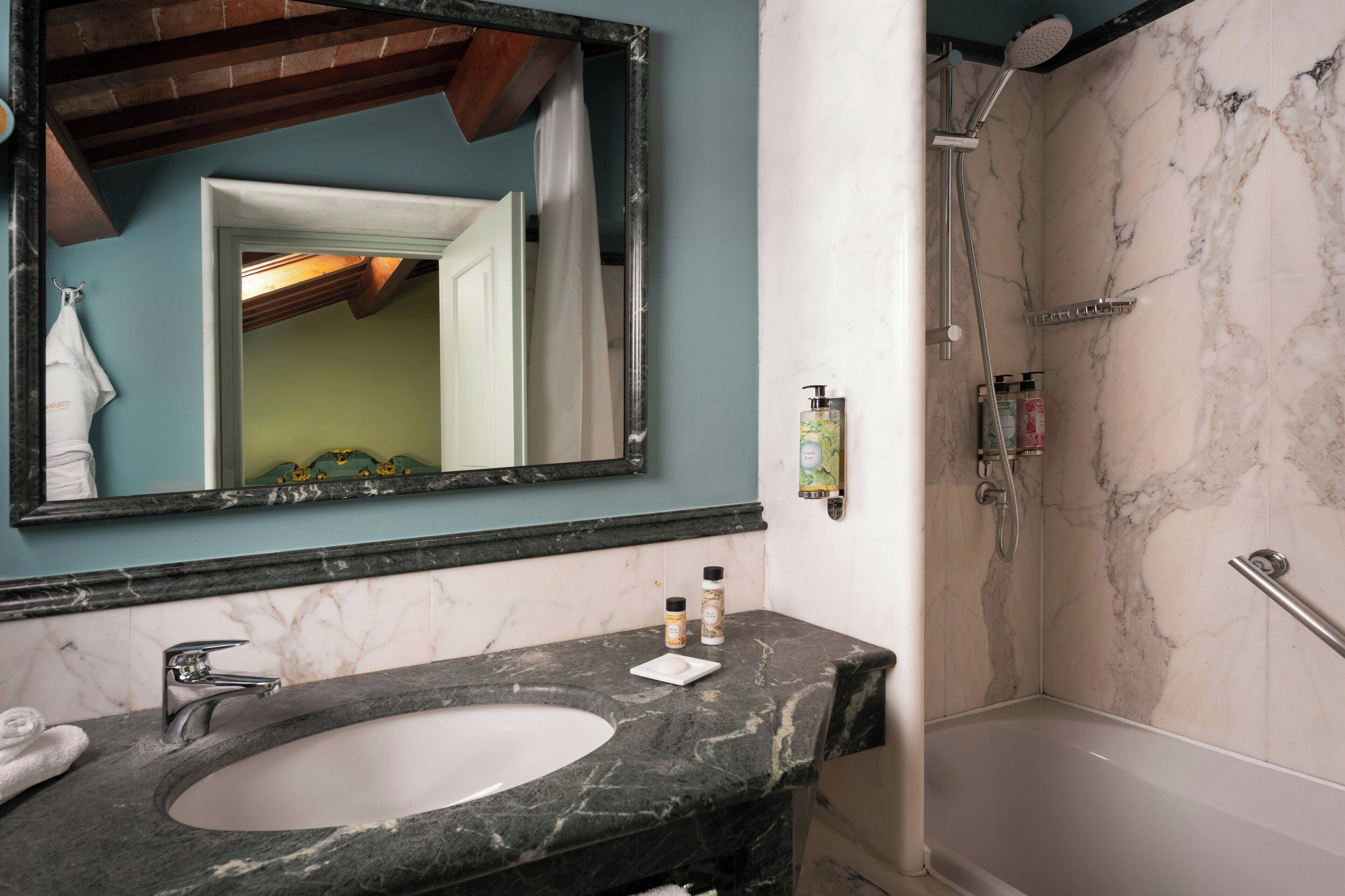 Une salle de bain avec un lavabo en marbre, un grand miroir, une douche avec un pommeau de douche amovible et un porte-serviettes.